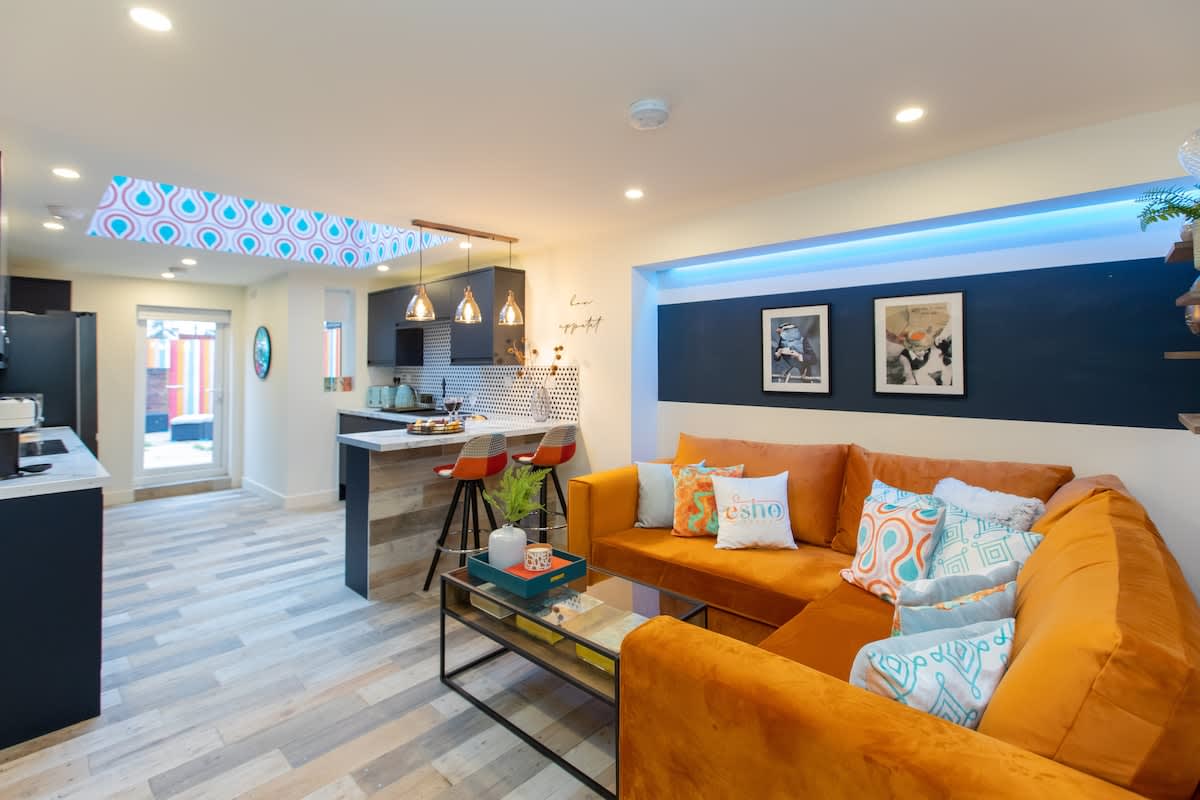 Orange corner sofa and open-plan kitchen in the five-bedroom en-suite Esho Stays house in Coventry