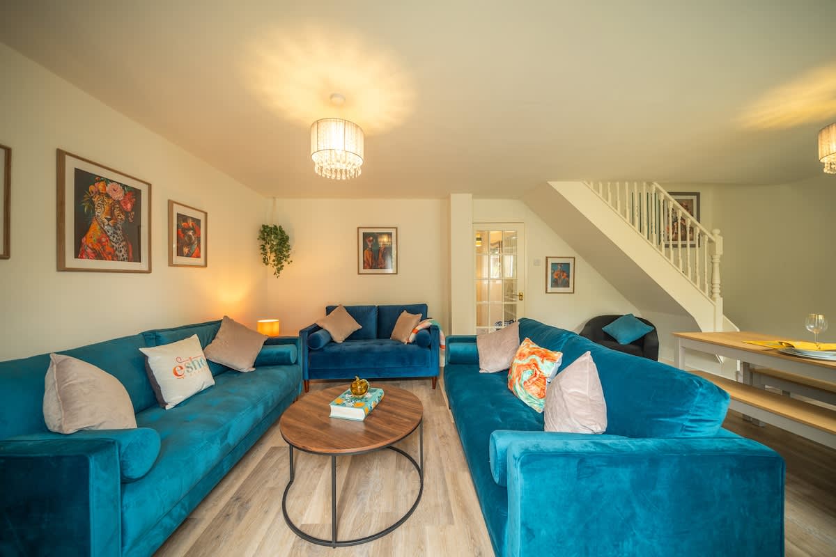 Teal velvet sofas and a staircase in the living room of the five-bedroom Esho Stays house in Cirencester