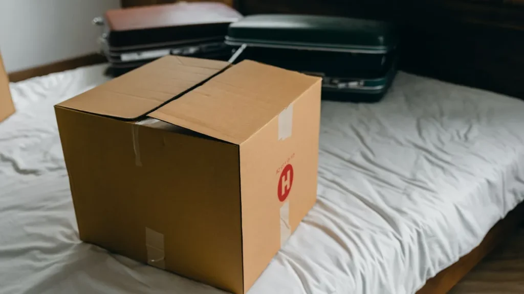 A cardboard box and suitcases on a bed in a temporary home, the first day in insurance claim accommodation in Gloucester