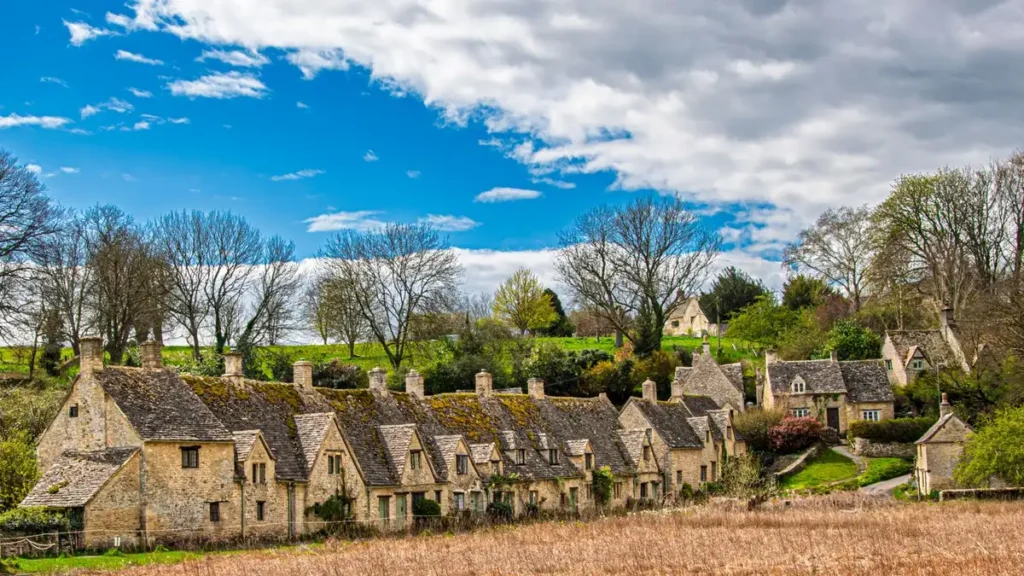 A long row of stone cottages under a blue sky in a Cotswold village, one of the best Cotswold villages to visit