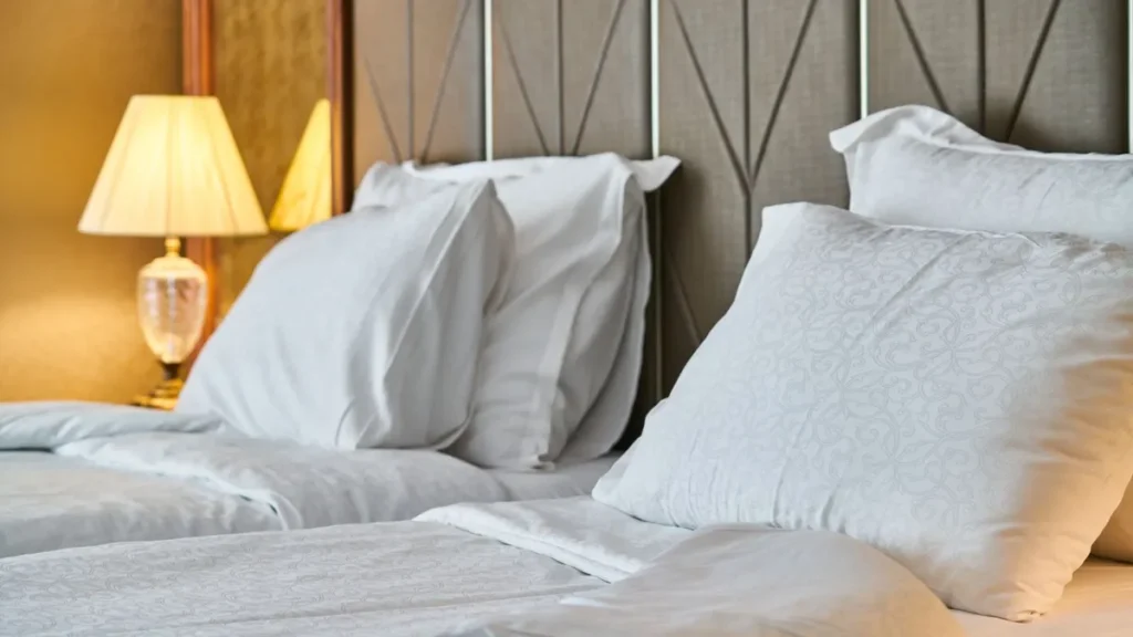 Made-up hotel twin beds with white pillows and a bedside lamp, the usual alternative to contractor accommodation